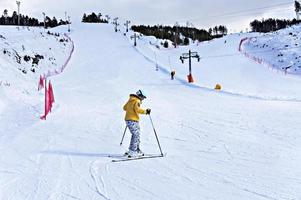 feliz sorridente jovem de jaqueta amarela e capacete de esqui esquiando em uma encosta de montanha, esportes de inverno, atividade ao ar livre de esqui alpino, estilo de vida saudável foto