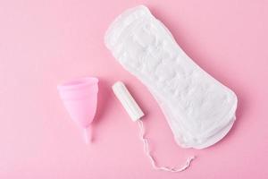 absorvente higiênico, copo menstrual e tampão em um fundo rosa foto