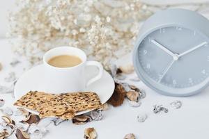 xícara de café e despertador clássico em uma mesa branca foto