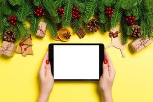vista superior da mulher segurando o tablet nas mãos em fundo amarelo feito de decorações de natal. conceito de férias de ano novo. brincar foto