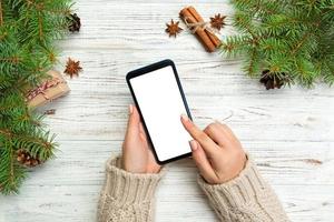 mãos femininas de fundo de natal mensagens smartphone no fundo da mesa de madeira rústica com decoração de natal. vista superior, configuração plana foto