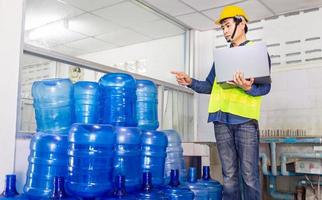 jovem trabalhador e inspetor de qualidade em uma fábrica verificando galões de água azul antes do envio para conter água potável. foto