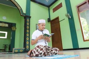 jovem muçulmano asiático orando na mesquita e lendo al quran foto