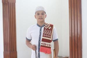 jovem muçulmano asiático orando na mesquita carregando um tapete de oração foto