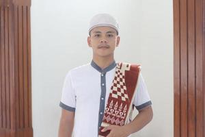 jovem muçulmano asiático orando na mesquita carregando um tapete de oração foto