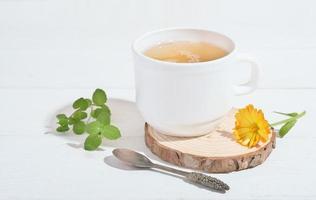 chá de ervas com calêndula e hortelã em uma mesa de madeira branca. medicina alternativa para a saúde do sistema gastrointestinal e alívio da ansiedade. bebida calmante e relaxante à noite. foto