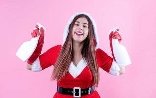 closeup de mulher caucasiana feliz vestindo roupas de papai noel e luvas de limpeza, segurando sprays de limpeza foto