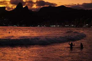 rio de janeiro, rj, brasil, 2022 - pessoas em silhueta assistem o pôr do sol na rocha do arpoador, praia de ipanema