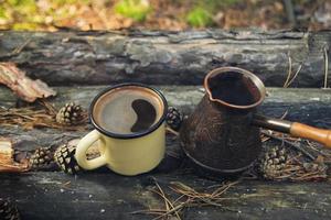 copo de metal amarelo com café quente e cezve no fundo de madeira com as moedas, agulhas e casca de árvore. foto