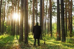 jovem com uma jaqueta preta está andando em uma floresta de pinheiros ao nascer do sol. foto