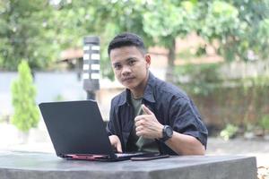 atraente jovem asiático usando laptop no espaço de coworking com cara de feliz foto