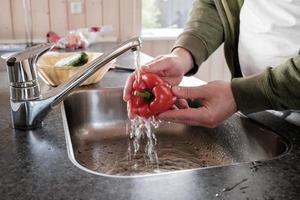 as mãos dos homens lavam os pimentões em água corrente, em uma pia. páprica fresca útil na cozinha. foto