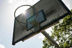 cesta de basquete no fundo do sol, céu e árvore. campo de esportes ao ar livre. conceito de um estilo de vida ativo. vista de baixo. foto