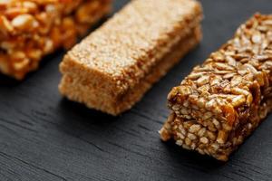 barra de granola de cereais com amendoim, gergelim e sementes de girassol em uma tábua sobre uma mesa de pedra escura. vista de cima. três barras variadas foto