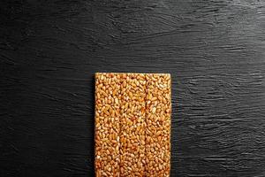 telha kozinaki de sementes de girassol em um fundo preto textural. deliciosos doces orientais gozinaki de sementes de girassol, sementes de gergelim e amendoim, cobertos com mel com uma cobertura brilhante foto