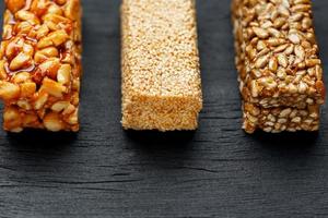 barra de granola de cereais com amendoim, gergelim e sementes de girassol em uma tábua sobre uma mesa de pedra escura. vista de cima. três barras variadas foto