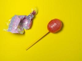 doce desembrulhado. pirulito em um fundo amarelo. caramelo no palito. não é comida saudável. foto