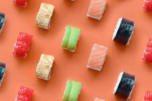 diferentes tipos de rolos de sushi asiáticos em fundo laranja. minimalismo vista superior plana padrão leigo com comida japonesa foto