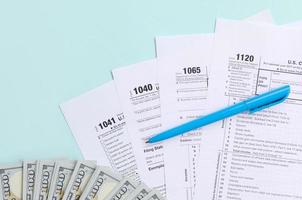 formulários de imposto fica perto de notas de cem dólares e caneta azul sobre um fundo azul claro. restituição do Imposto de Renda foto