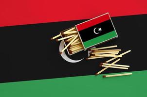 A bandeira da líbia é mostrada em uma caixa de fósforos aberta, da qual vários fósforos caem e fica em uma grande bandeira foto