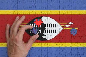 a bandeira da suazilândia é retratada em um quebra-cabeça, que a mão do homem completa para dobrar foto