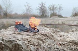 queima de tênis esportivos ou sapatos de ginástica em chamas na costa da praia. atleta queimado. esforço físico durante o conceito de treinamento foto