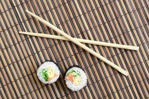 rolos de sushi e pauzinhos de madeira estão em uma esteira de serragem de palha de bambu. comida asiática tradicional. vista do topo. minimalismo plano leigo com espaço de cópia foto