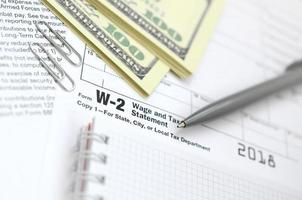 a caneta, o caderno e as notas de dólar estão no formulário de imposto w-2 salário e declaração de imposto. hora de pagar impostos foto