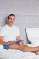 homem sorridente usando tablet pc na cama