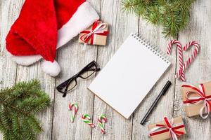 itens de natal e negócios com espaço de cópia recortado boné de papai noel óculos de caneta e caixa de presente decorada e abeto foto