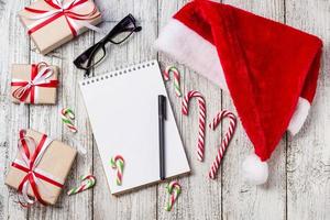 itens de natal e ano novo com espaço de cópia santa cap bloco de notas, óculos de caneta e caixas de presente decoradas foto