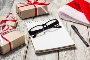 itens de natal e negócios com espaço de cópia santa cap bloco de notas, óculos de caneta e caixas de presente decoradas foto