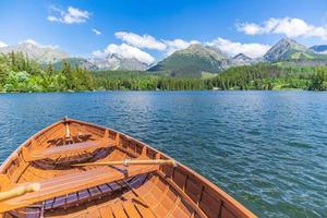 Lago de montanha com floresta de coníferas, céu azul ensolarado de barco de madeira, fundo de viagens de liberdade idílica. lugar turístico romântico. parque nacional high tatras, europa. bela paisagem natural vista idílica foto