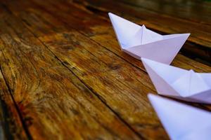 origami, barco de papel branco isolado em um piso de madeira. barquinhos de papel significam andar. sentimento de liberdade liderança foto