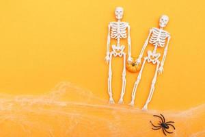 esqueletos com abóbora, teia de aranha e aranhas pretas em fundo laranja. conceito de halloween foto