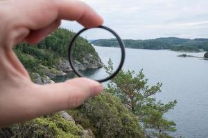 mão do fotógrafo coloca um filtro de polarização na câmera, tendo como pano de fundo uma bela paisagem do mar e das rochas. foto