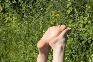 pés femininos descalços se aquecem ao sol em um dia quente de verão, contra o pano de fundo da vegetação. conceito de férias. foto