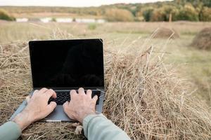 trabalho remoto com um laptop em um palheiro, no contexto de uma bela paisagem rural, em uma noite de verão. estilo de vida. foto