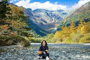 menina asiática com um belo fundo do parque nacional center kamikochi pela montanha de neve, rock e rio azusa da cobertura da colina com folha de mudança de cor durante a temporada de folhagem de outono. foto