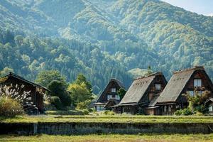 vila japonesa de shirakawago durante outubro na temporada de folhagem de outono. casa tradicional de shirakawa no telhado triangular com fundo de campo de arroz, montanha de pinheiros e céu de nuvens claras depois. foto