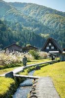 Japonês não identificado com um fundo de aldeia de shirakawago durante o outono com uma casa de triângulo, campo de arroz e montanha de pinheiros. foto