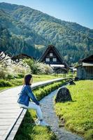 linda garota japonesa com um fundo de aldeia de shirakawago durante o outono com uma casa de triângulo, campo de arroz e montanha de pinheiros. foto