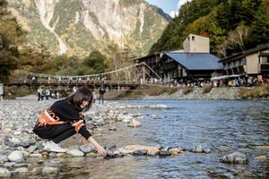 menina asiática contar rio rock com um belo fundo do centro do parque nacional de kamikochi pela montanha de neve, rocha, rio azusa da cobertura da colina com folha de mudança de cor durante a temporada de folhagem de outono. foto