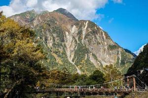 kamikochi, nagano, japão - outubro de 2022 prazer de turistas não identificados na ponte kappa bashi na área do ponto central do parque nacional de kamikochi durante a temporada de folhagem de outono. foto