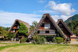 vila japonesa de shirakawago durante outubro na temporada de folhagem de outono. casa tradicional de shirakawa no telhado triangular com fundo de campo de arroz, montanha de pinheiros e céu de nuvens claras depois. foto