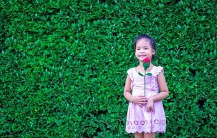 menina bonita com vestido, segurando uma rosa vermelha no parque foto