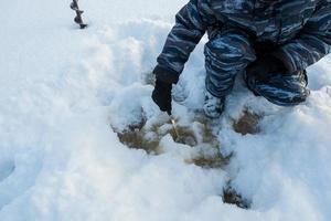 pescador remove gelo de um buraco com uma colher, uma broca fica nas proximidades. preparando-se para a pesca de inverno. passatempos e estilo de vida. foto