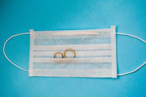 anéis de casamento de ouro estão em uma máscara médica protetora descartável para proteção contra doenças mortais perigosas de micróbios e vírus pelo coronavírus covid-19 em um fundo azul foto