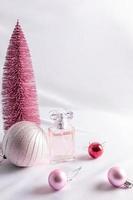 um frasco de perfume feminino de aroma delicado contra uma árvore de natal rosa e bolas. o conceito de anunciar um presente de fragrância. foto