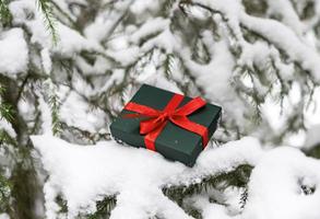 presente na caixa verde com fita vermelha na árvore de abeto nevado no fundo de natal da floresta de inverno e feriados de ano novo foto